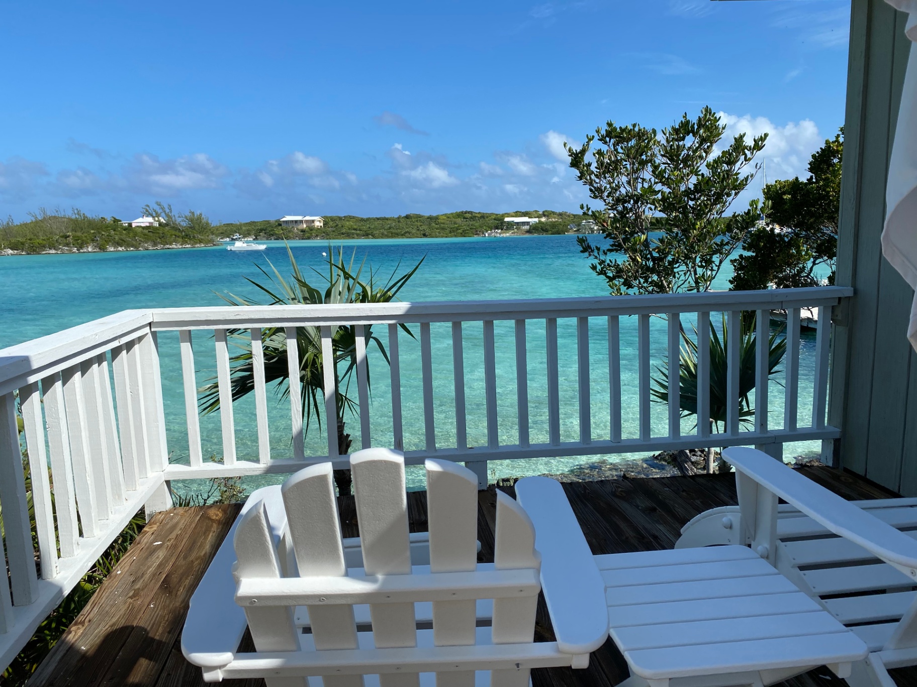 White Adirondack chairs on a wooden deck overlooking aqua water